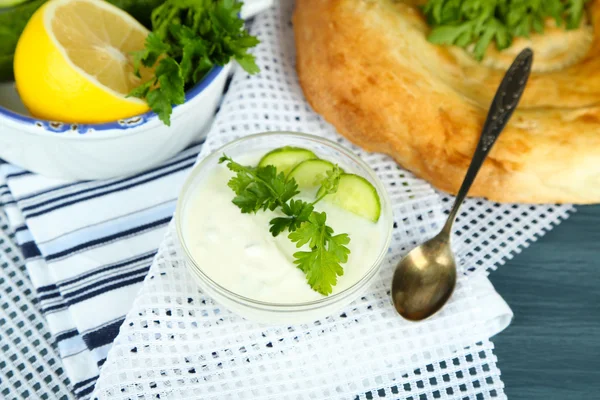 Cucumber yogurt in glass bowl and homemade bread, on color napkin, on wooden background — Stock Photo, Image