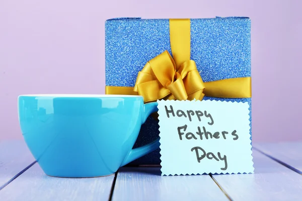 Etiqueta del Día de los Padres Felices con caja de regalo y taza, sobre mesa de madera, sobre fondo claro —  Fotos de Stock