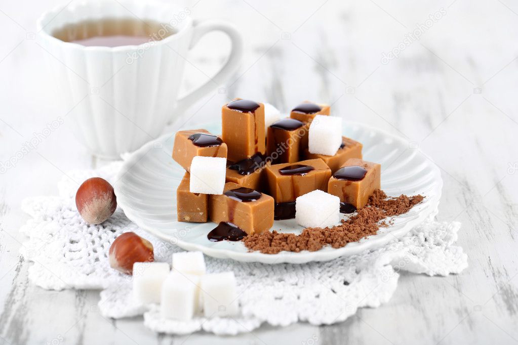 Many toffee on plate and cup of tea on napkin on wooden table