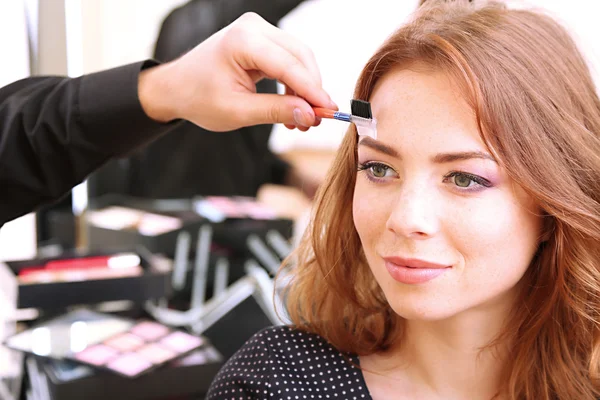 Joven estilista haciendo maquillaje hermosa mujer en salón de belleza —  Fotos de Stock