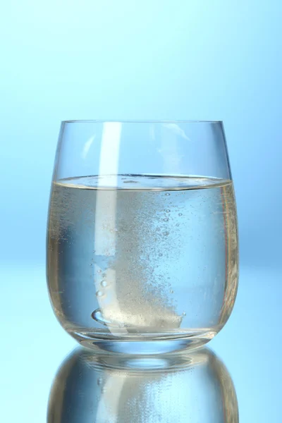 Kaca dengan tablet efervescent dalam air dengan gelembung di latar belakang biru — Stok Foto