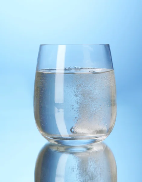 Sklo s efervescent tablet ve vodě s bublinkami na modrém pozadí — Stock fotografie