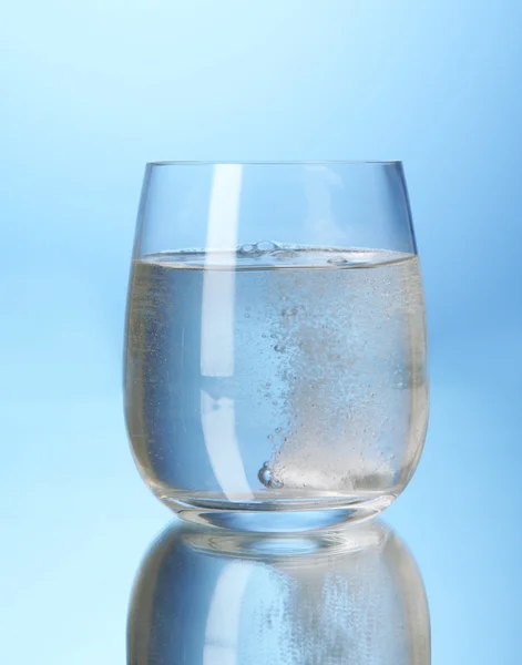 Glas med efervescent tablett i vatten med bubblor på blå bakgrund — Stockfoto