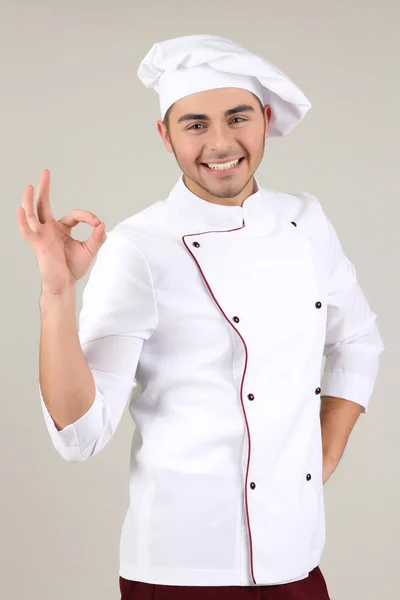 Professionele chef-kok in het witte uniform en hoed, op grijze achtergrond — Stockfoto