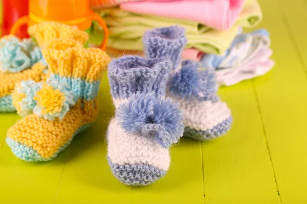 Composition with crocheted booties for baby,clothes, bottles on wooden background — Stock Photo, Image