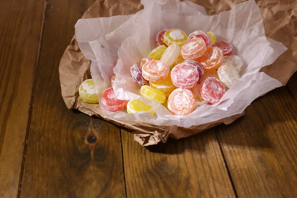 Doces multicoloridos doces no papel, no fundo de madeira — Fotografia de Stock