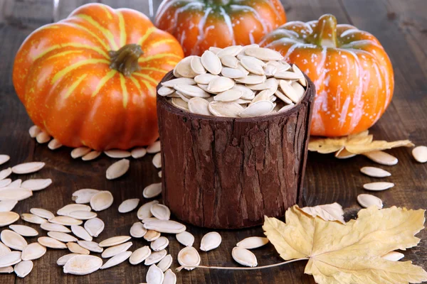 Semillas de calabaza en maceta con calabazas sobre fondo de madera — Foto de Stock