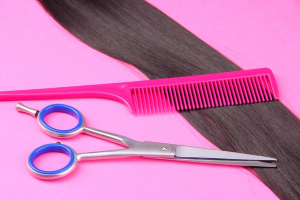 Длинные черные волосы с расческой и ножницами на розовом фоне — стоковое фото
