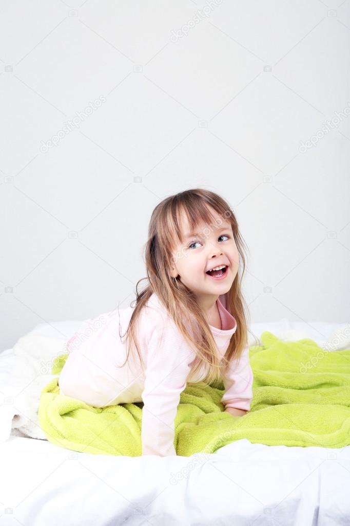 Little girl sitting on bed on wall background