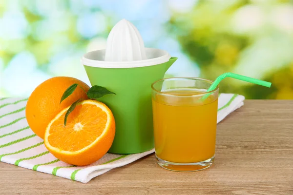 Imprensa de citrinos, copo de suco e laranjas maduras na mesa de madeira marrom — Fotografia de Stock