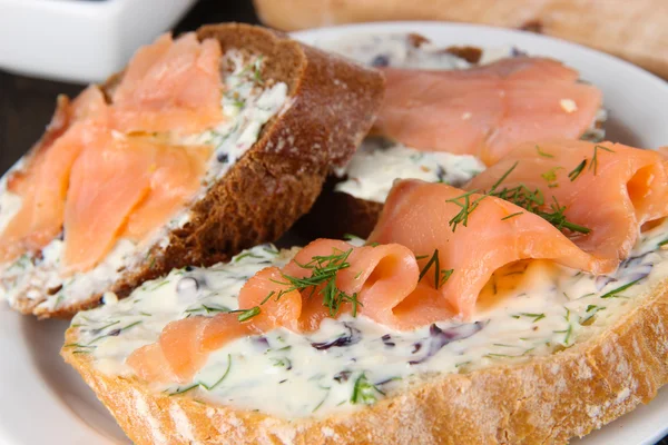 Vissen broodjes op snijplank en plaat op houten tafel — Stockfoto