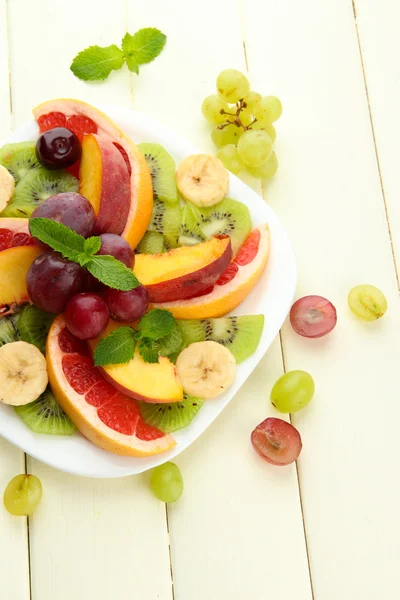 Surtido de frutas en rodajas en plato, sobre mesa de madera blanca — Foto de Stock