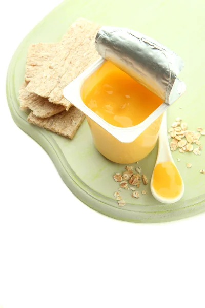 Sabroso yogur en copa de plástico abierta, galletas y fruta, sobre tabla de madera, aislado en blanco —  Fotos de Stock