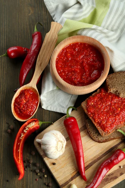 Composition with salsa sauce on bread,, red hot chili peppers and garlic, on napkin, on wooden background — Stock Photo, Image