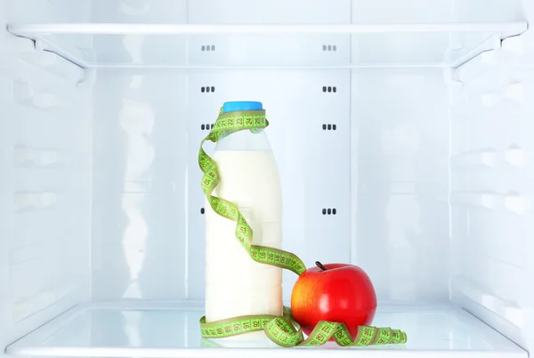 Conceptual photo of diet: apple and milk bottle with measuring type on shelf of refrigerator — Stock Photo, Image