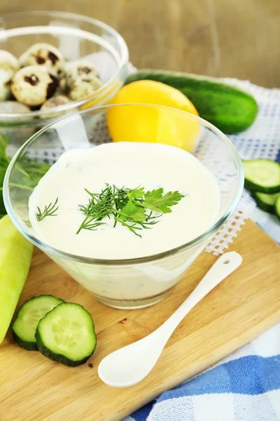 Yogur de pepino en un tazón de vidrio, en una servilleta de color, sobre un fondo de madera —  Fotos de Stock