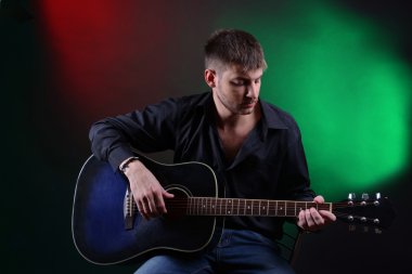 genç müzisyen akustik gitar çalıyor ve şarkı söyleme, koyu renk arka plan üzerinde