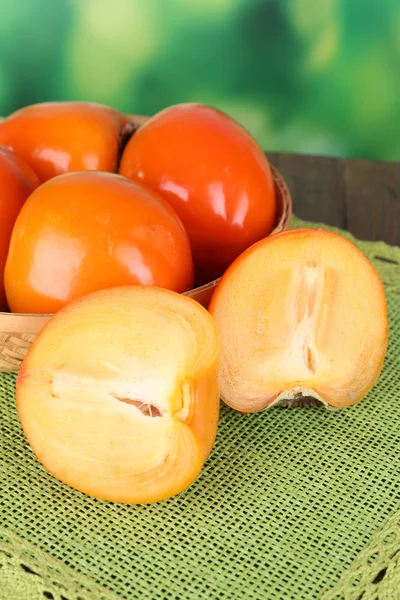 Ripe persimmons in wicker basket on table on bright background — Stock Photo, Image