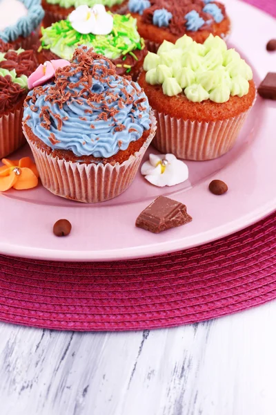 Mumsiga muffins med smörkräm, på plattan, på färg Servett, på färg trä bakgrund — Stockfoto