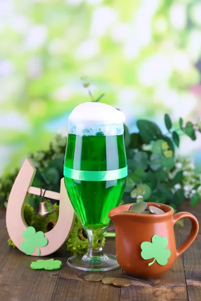 Glass of green beer, pitcher with coins and horseshoe on natural background close-up — Stock Photo, Image