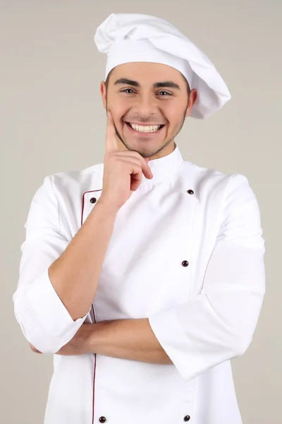 Professionele chef-kok in het witte uniform en hoed, op grijze achtergrond — Stockfoto