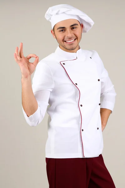 Chef profesional en uniforme blanco y sombrero, sobre fondo gris — Foto de Stock