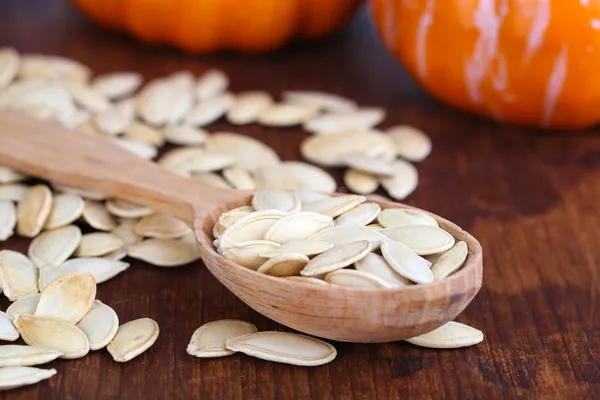 Pumpkin seeds in spoon with pumpkins on wooden background — Stock Photo, Image