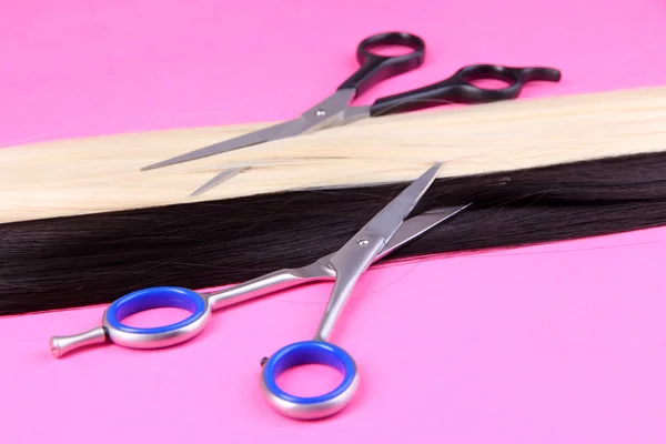 Long black and blond hair with scissors on pink background — Stock Photo, Image