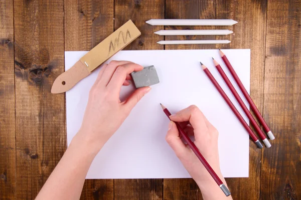 Hände halten Bleistift und Radiergummi mit Kunstmaterialien auf Holzgrund — Stockfoto