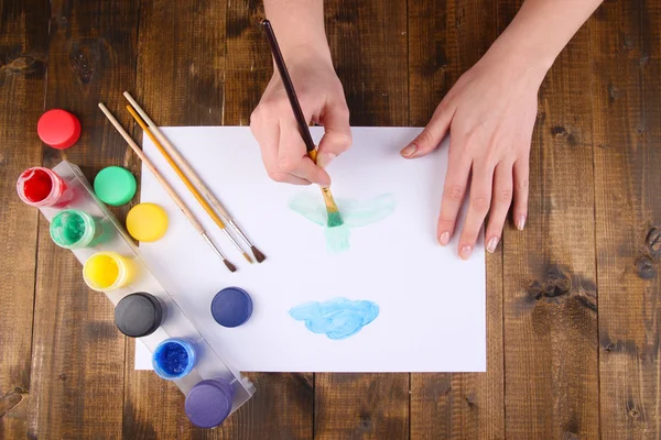 Hand holding brush with paints and paper on wooden background — Stock Photo, Image