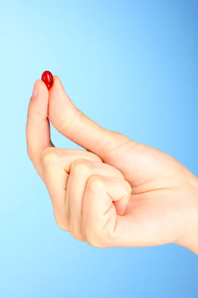 A mão da mulher segurando uma pílula vermelha no fundo azul close-up — Fotografia de Stock