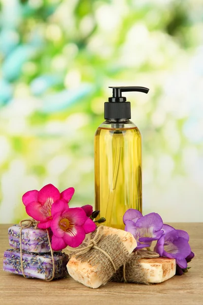 Liquid and hand-made soaps on wooden table, on green background — Stock Photo, Image