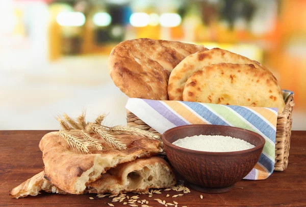 Pita breads in basket with spikes and flour on table on bright background — Stock Photo, Image