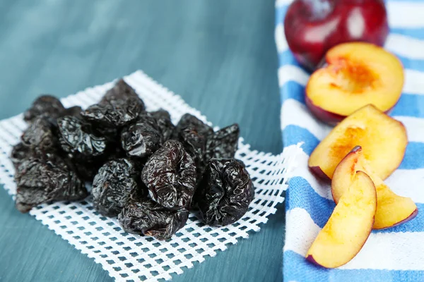 Fresh and dried plums on napkin, on wooden background — Stock Photo, Image