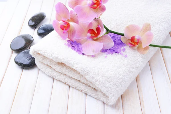 Still life with beautiful blooming orchid flower, towel and bowl with sea salt, on color wooden background — Stock Photo, Image