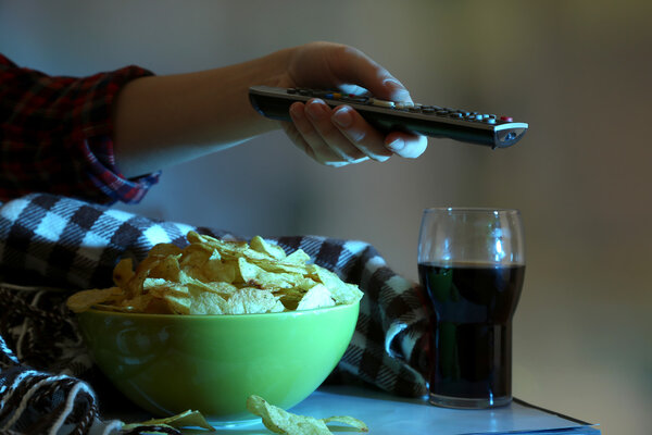 Кто-то смотрит телевизор с чипсами и колой в комнате
