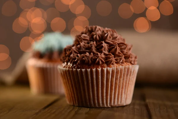 Sabrosos cupcakes con crema de mantequilla, sobre mesa de madera, sobre fondo de luces —  Fotos de Stock