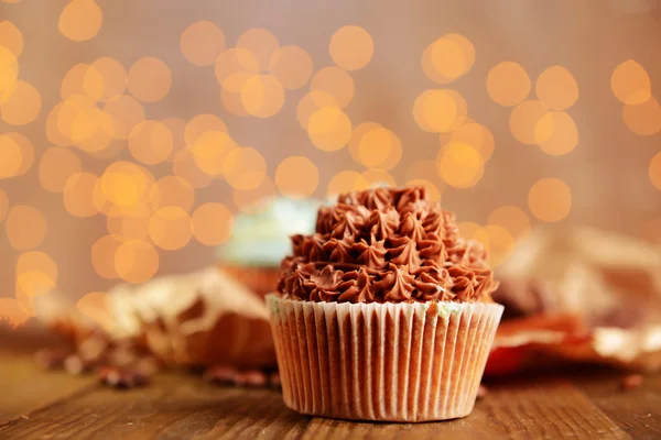 Sabrosos cupcakes con crema de mantequilla, sobre mesa de madera, sobre fondo de luces —  Fotos de Stock