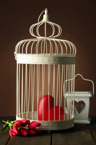 Herz in dekorativem Käfig auf Holztisch, auf braunem Hintergrund — Stockfoto