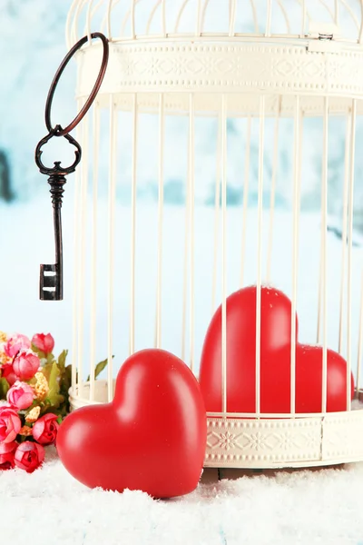 Herzen im dekorativen Käfig auf winterlichem Hintergrund — Stockfoto