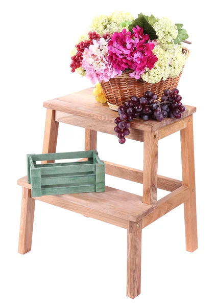 Wicker basket with flowers and fruits, on small wooden ladder, isolated on white — Stock Photo, Image