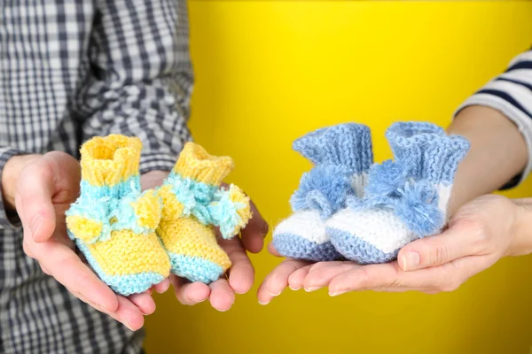 Hands with crocheted booties for baby, on color background — Stock Photo, Image