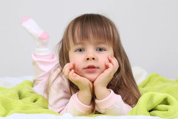 Kleines Mädchen liegt auf Bett auf Wandhintergrund — Stockfoto