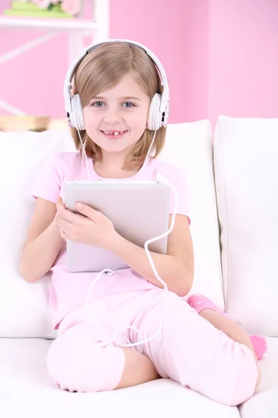 Little girl listening music sitting on sofa in room — Stock Photo, Image