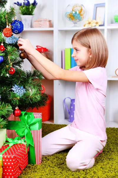 Niña sentada cerca del árbol de Navidad en la habitación — Foto de Stock