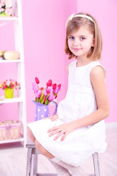 Meisje, zittend op kleine ladder met bloemen op roze achtergrond — Stockfoto