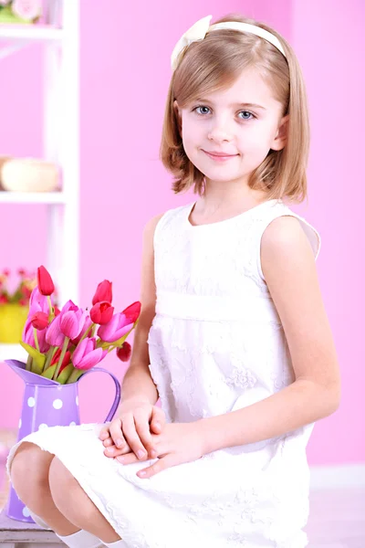 Little girl sitting on small ladder with flowers on pink background — Stock Photo, Image