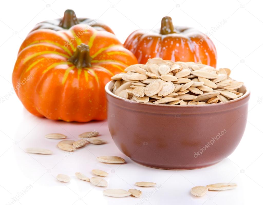 Pumpkin seeds in bowl with pumpkins isolated on white