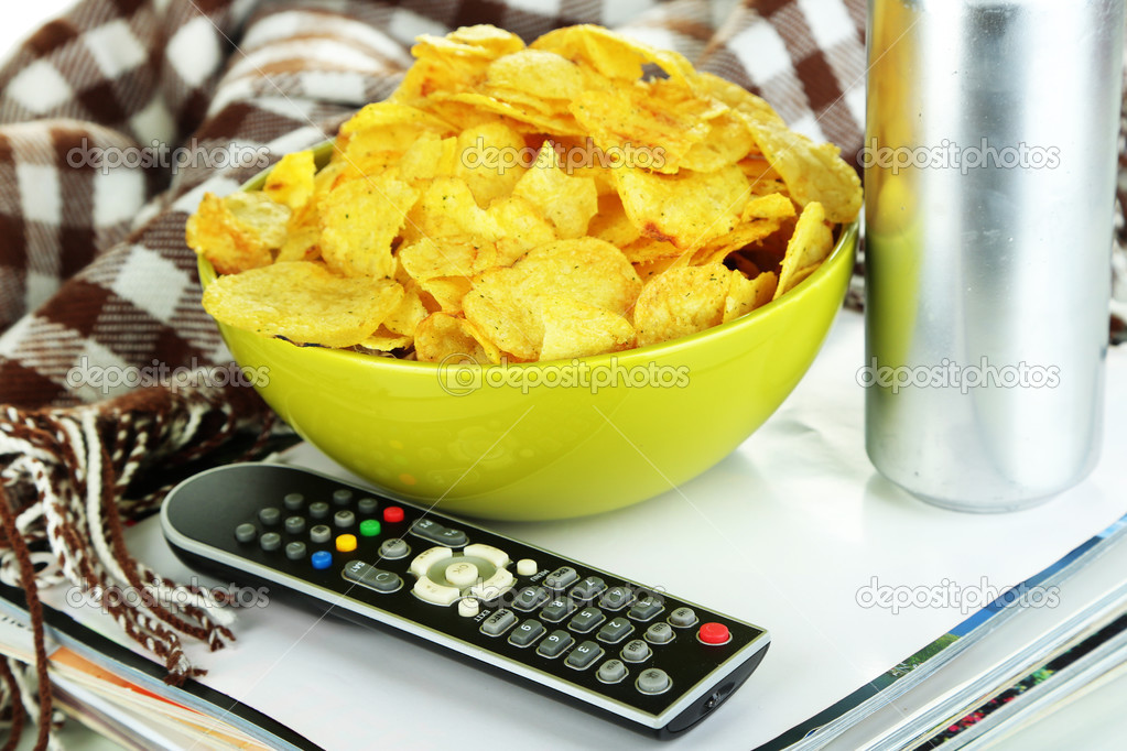 Chips in bowl, magazines, plaid and TV remote close-up