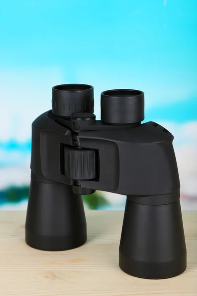 Black modern binoculars on wooden table on blue background — Stock Photo, Image